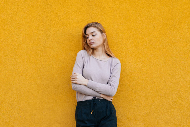 cute young blonde girl in trendy clothes posing against yellow wall, street style - Foto, imagen