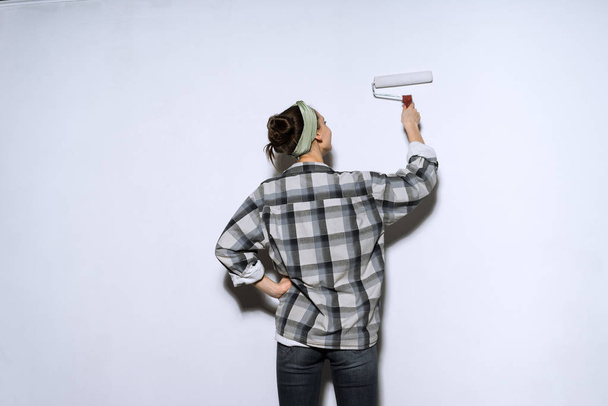 young girl in plaid shirt colors the wall with a platen in white color - Zdjęcie, obraz