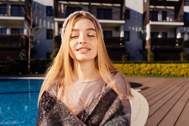 gelukkig lachend meisje Blond in een roze hoed zit bij het blauwe zwembad, geniet van de zon en warmte - Foto, afbeelding
