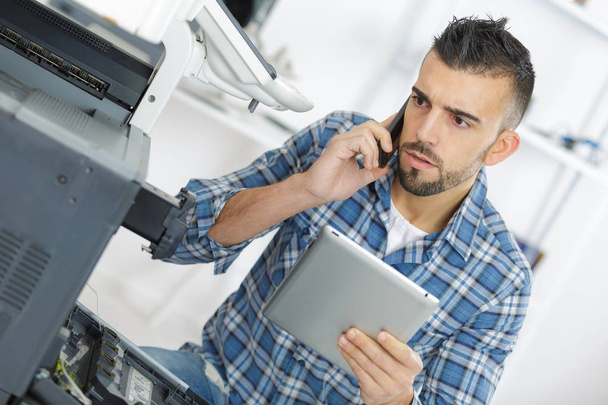 technician seeking help on the phone while repairing printer - Fotoğraf, Görsel