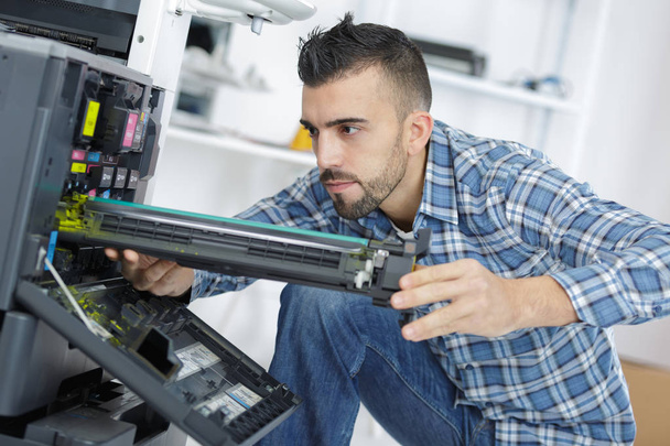 νεαρός άνδρας τεχνικός επισκευάζει ψηφιακό φωτοτυπικό μηχάνημα - Φωτογραφία, εικόνα