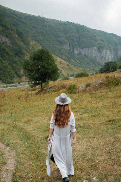 Een meisje in een hoed wandelingen in de buurt van de bergen - Foto, afbeelding