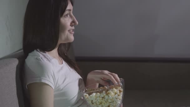 Young woman alone watching a movie in the evening with popcorn - Filmagem, Vídeo