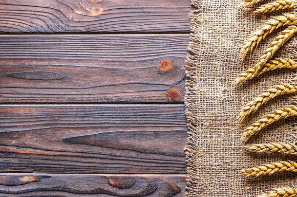 Wheat ears border on old burlap on wooden background - Foto, afbeelding