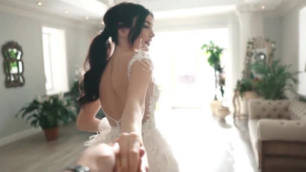 Volg me. een heel mooi meisje in een witte elegante jurk leidt de exploitanten hand aan het licht. charmante jongedame met feestelijke make-up en kapsel. Slow motion - Video