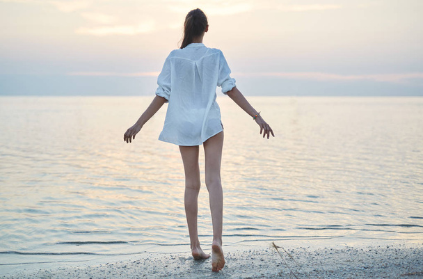 beautiful sexual woman in white shirt and bikini walking on the beach against the sea and sunset - Foto, Bild