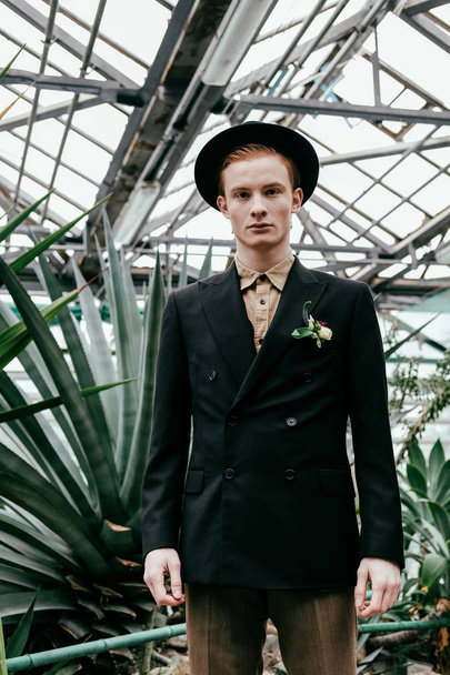 portrait of handsome red hair man in hat looking at camera in greenhouse  - Photo, Image