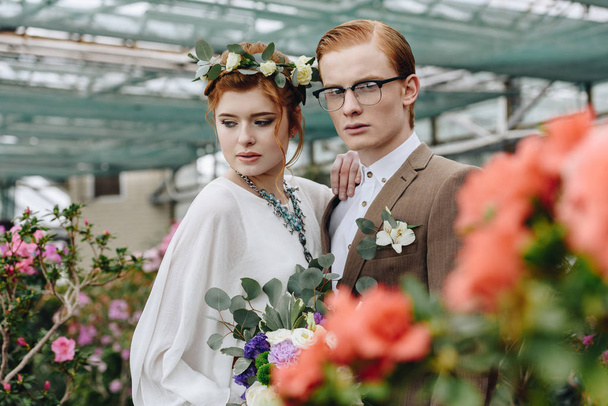 schöne junge Bräutigam und Braut mit Brautstrauß stehen zusammen im botanischen Garten  - Foto, Bild