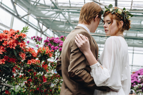 beautiful young elegant wedding couple embracing between flowers in botanical garden  - Photo, Image