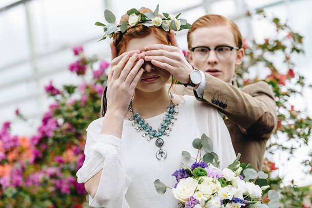 young man in eyeglasses closing eyes to beautiful redhead bride with wedding bouquet - Zdjęcie, obraz