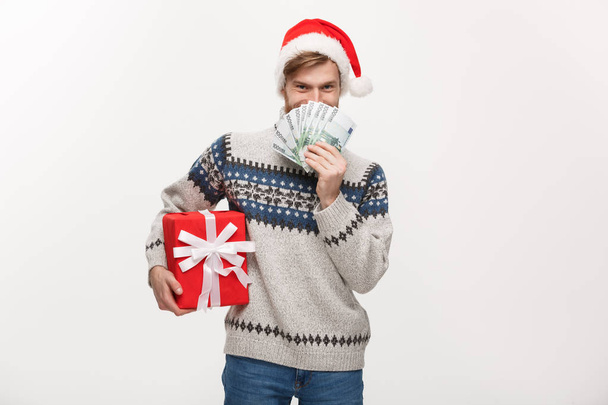 Concept de vacances - jeune homme barbe tenant une boîte cadeau de Noël et de l'argent sur fond blanc
 - Photo, image