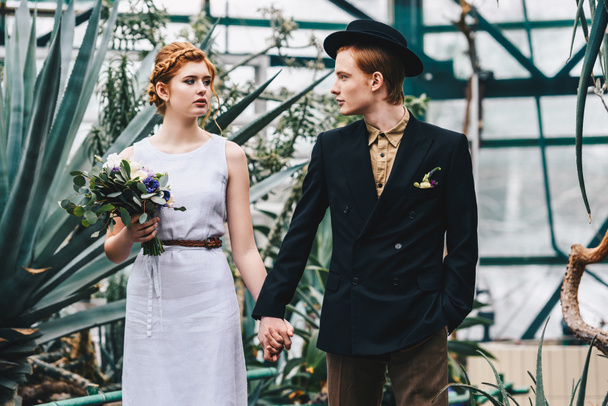 krásná mladá svatební pár, drželi se za ruce a při pohledu na sebe v botanické zahradě - Fotografie, Obrázek