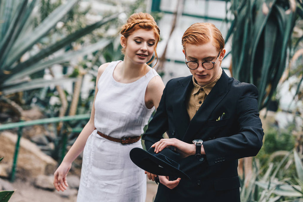 beautiful young redhead wedding couple looking at wristwatch in botanical garden - Photo, image