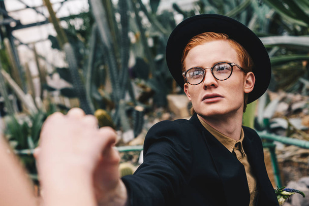 cropped shot of stylish young man in hat and eyeglasses making proposal to girl in botanical garden - Fotoğraf, Görsel