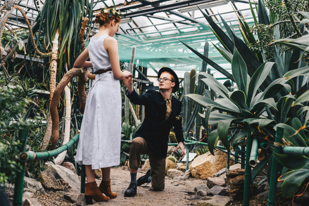 jeune homme avec boîte à bijoux debout sur le genou et tenant la main de belle jeune femme dans le jardin botanique
  - Photo, image