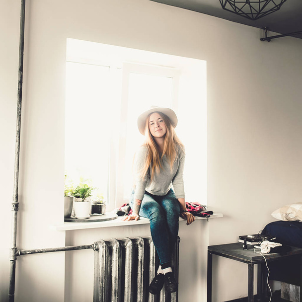 young fashion woman with red hair in hat sitting on windowsill on window background - Foto, imagen