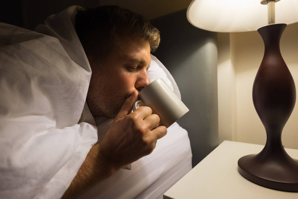 Doente caucasiano homem maduro beber a água na cama closeup à noite
. - Foto, Imagem