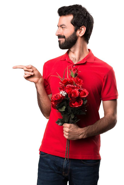 Красивий чоловік тримає квіти, вказуючи на бічний фон
 - Фото, зображення