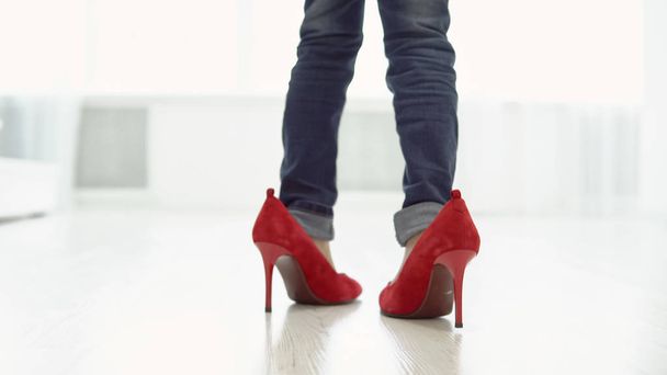 Κοριτσάκι σε κόκκινα παπούτσια της μητέρας είναι το περπάτημα γύρω από το σπίτι. Πίσω όψη - Φωτογραφία, εικόνα