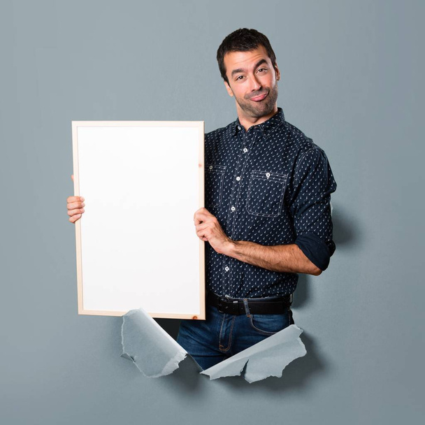 Happy Brunette man holding an empty placard through a paper hole - Photo, image