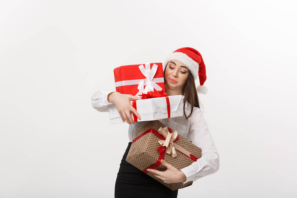 Бизнес - молодая кавказка, деловая женщина в шляпе санта, держащая в руках чересчур много подарочных коробок с беспокойным лицом
. - Фото, изображение