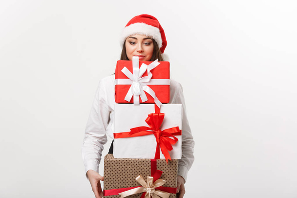 Geschäftskonzept - Schöne junge kaukasische Geschäftsfrau mit Weihnachtsmütze, die eine Menge Weihnachtsgeschenkboxen mit Kopierplatz auf der Seite hält. - Foto, Bild