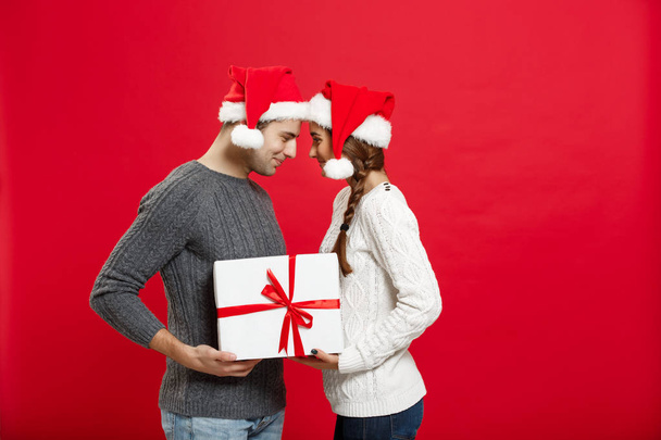 Christmas Concept - isolated lovely young couple holding tight with white gift over red background - Fotó, kép