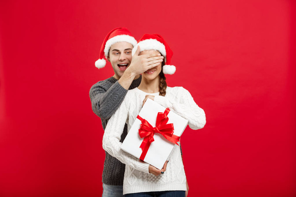 Різдвяна концепція - красивий молодий хлопець в светрі здивує свою дівчину білим подарунком
 - Фото, зображення