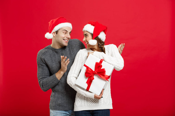 Weihnachtskonzept - schöner junger Freund im Pullover überrascht Freundin mit weißem Geschenk - Foto, Bild