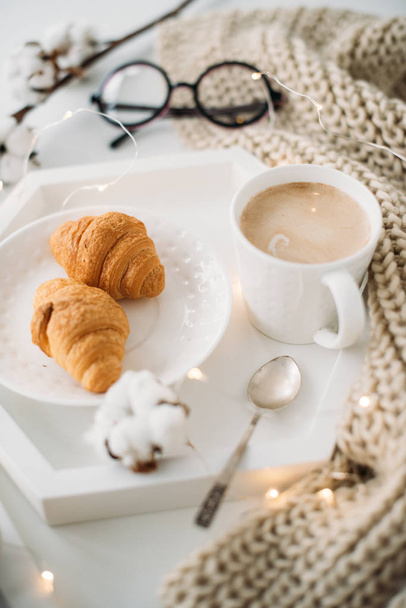 Acogedor desayuno casero, manta caliente, café y croissant en blanco
 - Foto, Imagen