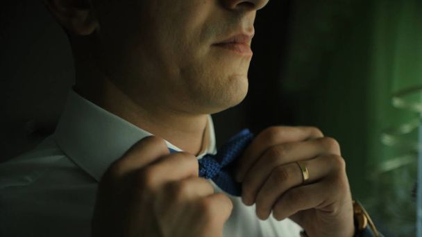 Man adjusting bow tie. Clip. Close-up of young man in white shirt adjusting his bowtie while standing - Photo, Image