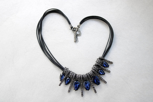 Hart gemaakt van vrouwelijke sieraden, kettingen met zwarte draden blauw juwelen, diamant, diamanten in de vorm van een hart op een lichtgrijze achtergrond. - Foto, afbeelding