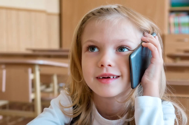 Un estudiante de primer grado en la escuela habla por teléfono. emociones de las colegialas
 - Foto, Imagen