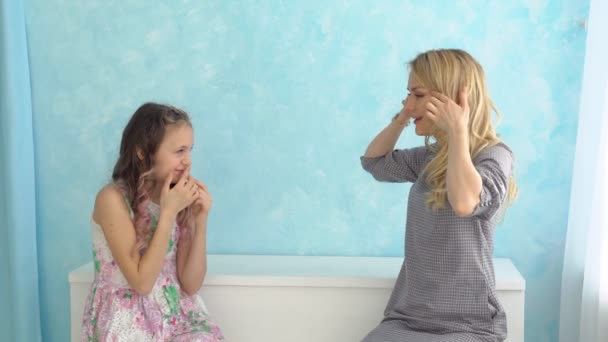 Anne ve kızı yan yana oturuyorlar ve mavi duvara karşı yüzlere kıvranmak - Video, Çekim