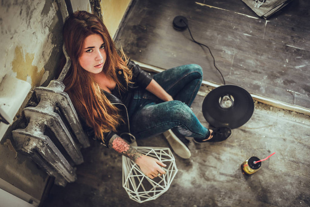 portrait of young fashion woman with red hair and tattoo in black clothes sitting on floor at loft style room.  - Foto, imagen