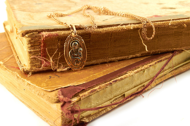 Стародавні книги. Золотий ланцюжок з кулоном Богородиці на тлі старого побоям книг - Фото, зображення
