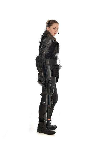 Pełna długość Portret żołnierz Kobieta w czarnej zbroi taktyczne, trzymając pistolet karabin, na białym tle na tle białego studia. - Zdjęcie, obraz