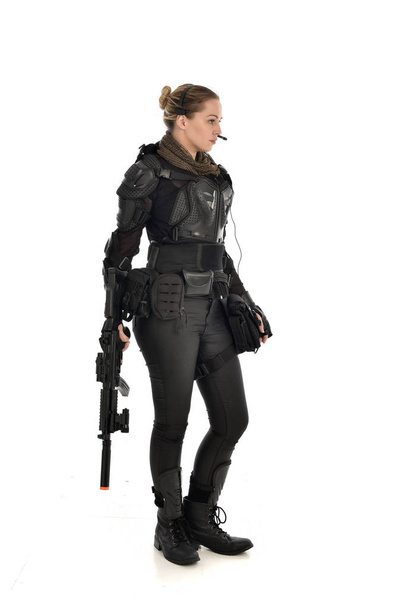 Ganzes Porträt einer Soldatin in schwarzer taktischer Rüstung, die ein Gewehr in der Hand hält, isoliert auf weißem Studiohintergrund. - Foto, Bild