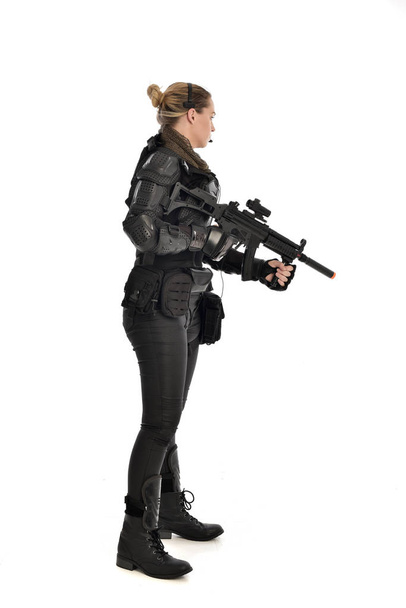 full length portrait of female  soldier wearing black  tactical armour, holding a rifle gun, isolated on white studio background. - Фото, изображение