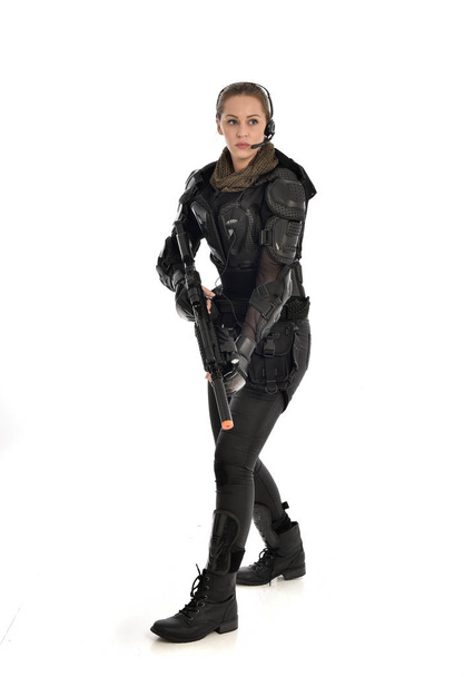portrait complet d'une femme soldat portant une armure tactique noire, tenant un fusil, isolée sur fond de studio blanc
. - Photo, image