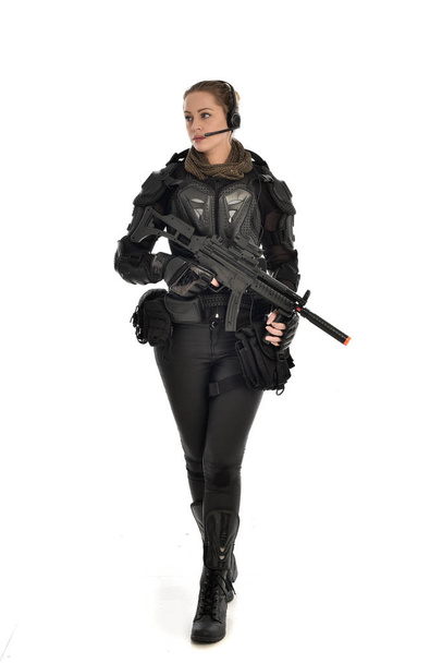 full length portrait of female  soldier wearing black  tactical armour, holding a rifle gun, isolated on white studio background. - Photo, Image
