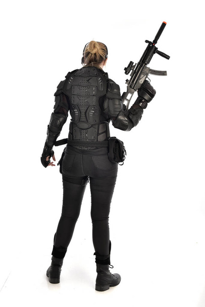 full length portrait of female  soldier wearing black  tactical armour, holding a rifle gun, isolated on white studio background. - Foto, Imagem