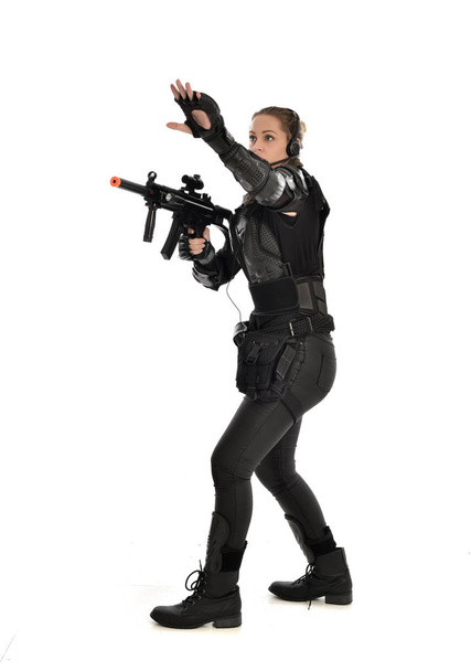 retrato de cuerpo entero de una soldado vestida con armadura táctica negra, sosteniendo una pistola de rifle, aislada sobre fondo blanco del estudio
. - Foto, imagen