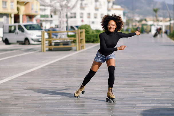 Black woman on roller skates riding outdoors on urban street - Foto, afbeelding