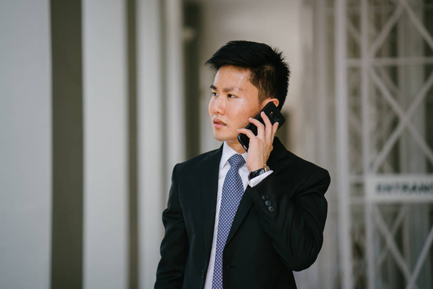 Portrait of a young handsome businessman dressed in a formal suit and tie.. He is is looking down at his smartphone. He looks smart and confident. - Foto, Bild