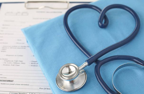een stethoscoop vormgeving een hart en een Klembord op een medische uniforme, close-up - Foto, afbeelding
