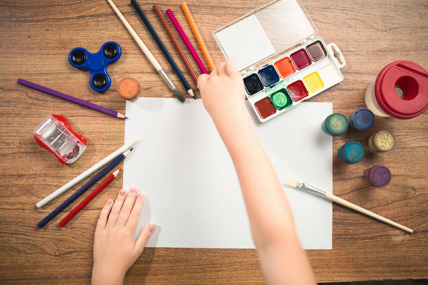 Χαριτωμένο παιδί χρωματίζει με χρωματιστά μολύβια σε χαρτί το top view - Φωτογραφία, εικόνα