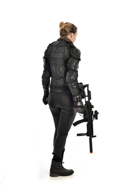 Pełna długość Portret żołnierz Kobieta w czarnej zbroi taktyczne, trzymając pistolet karabin, na białym tle na tle białego studia. - Zdjęcie, obraz