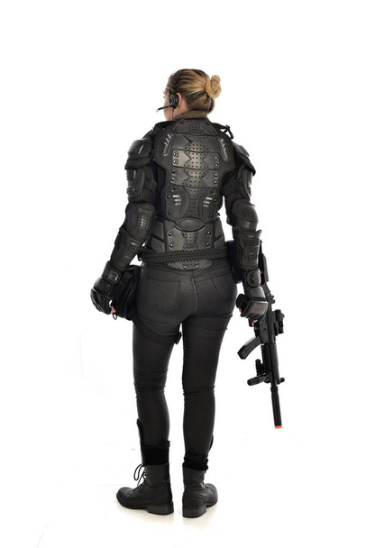 volledige lengte portret van vrouwelijke soldaat het dragen van zwarte tactische armour, houdt een pistool geweer, geïsoleerd op witte studio achtergrond. - Foto, afbeelding