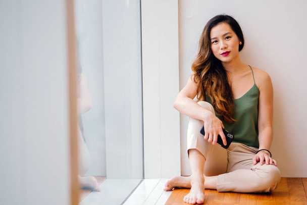 Retrato de uma jovem e atraente mulher chinesa (asiática) de Singapura sentada ao lado de uma janela em seu apartamento pela manhã
. - Foto, Imagem